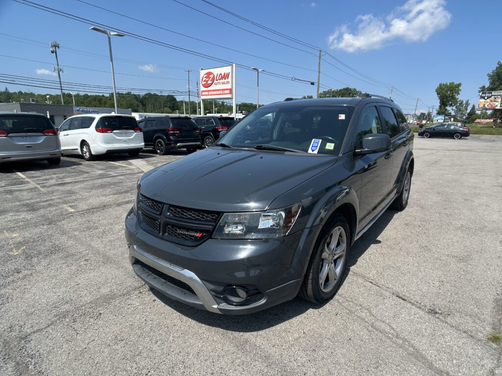Front-right view of a gray Dodge SUV in a car dealership lot, with an EZ LOAN Auto Sales sign in the background under a blue sky.