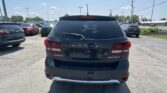 Rear view of a black Dodge Journey Crossroad SUV in a busy parking lot with other vehicles nearby under a clear blue sky