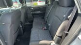 Rear passenger seating in a dark cloth SUV, three-seat row with headrests and buckled seat belts; outside cars visible through the windows.