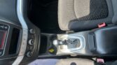 Front interior of a car showing the center console with gear shifter, climate controls, and a patterned black seat nearby.
