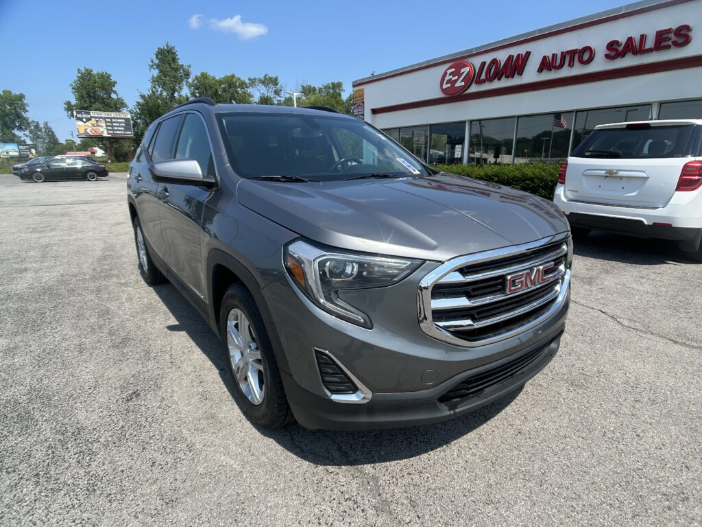 Gray GMC SUV in foreground at a car dealership lot with EZ Loan Auto Sales sign on the building in the background.