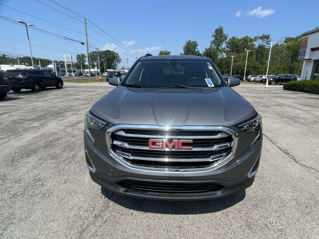 Front view of a gray GMC SUV in a sunny dealership lot, with other vehicles and a blue sky in the background.