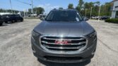 Front view of a gray GMC SUV in a sunny dealership lot, with other vehicles and a blue sky in the background.