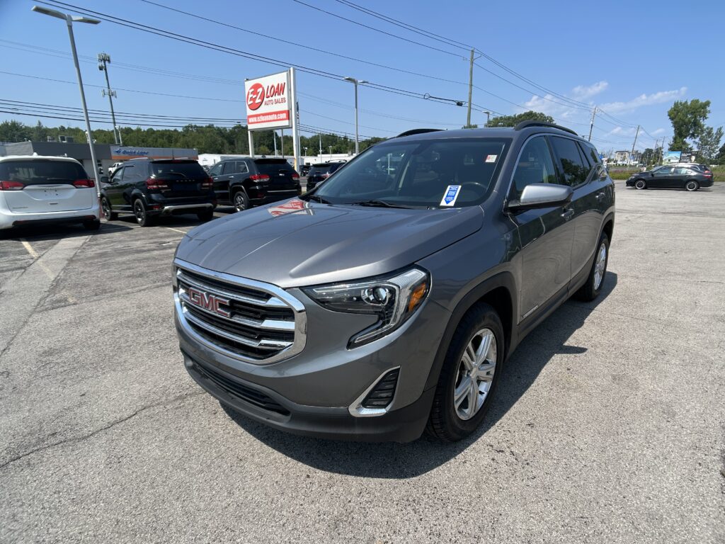 Gray GMC SUV in the foreground of a car dealership lot, with other vehicles and an EZ Loan Auto Sales sign in the background.