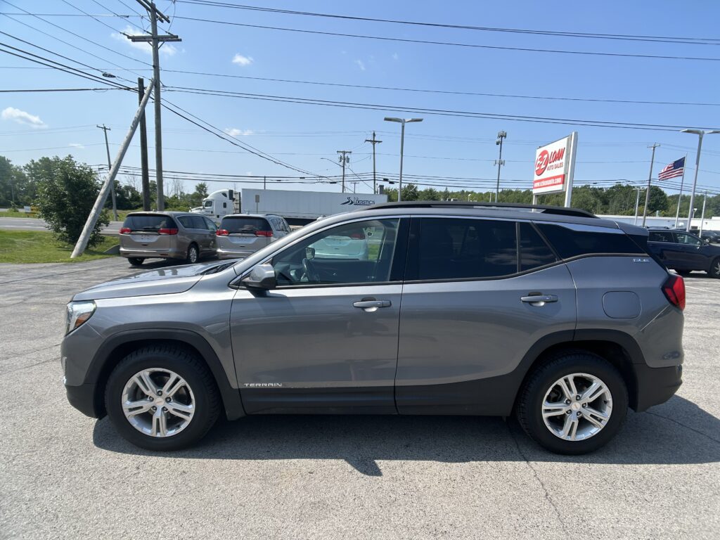 Gray GMC Terrain SUV in foreground of a car lot with overhead power lines and an EZ Auto Sales sign in the distance.