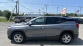 Gray GMC Terrain SUV in foreground of a car lot with overhead power lines and an EZ Auto Sales sign in the distance.