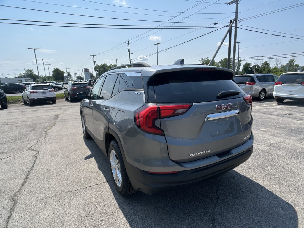 Rear view of a gray GMC Terrain SUV in a car dealership lot with other vehicles and overhead power lines in the background