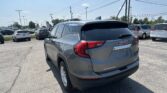 Rear view of a gray GMC Terrain SUV in a car dealership lot with other vehicles and overhead power lines in the background