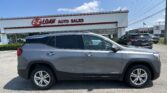 Gray GMC Terrain SUV parked in front of an E-Z Loan Auto Sales storefront on a sunny day with blue sky, other cars visible in the lot and a Toyota dealership in the background