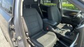 Inside a car with front seats and center console visible, driver’s door open and view of exterior parking lot.