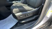 Front interior of a car showing a black fabric seat, center console with cupholders, and a paper floor mat.