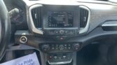 Car interior with center touchscreen displaying FM radio (96.9) and climate controls, seen from the driver’s seat, with a parking lot outside through the windshield.