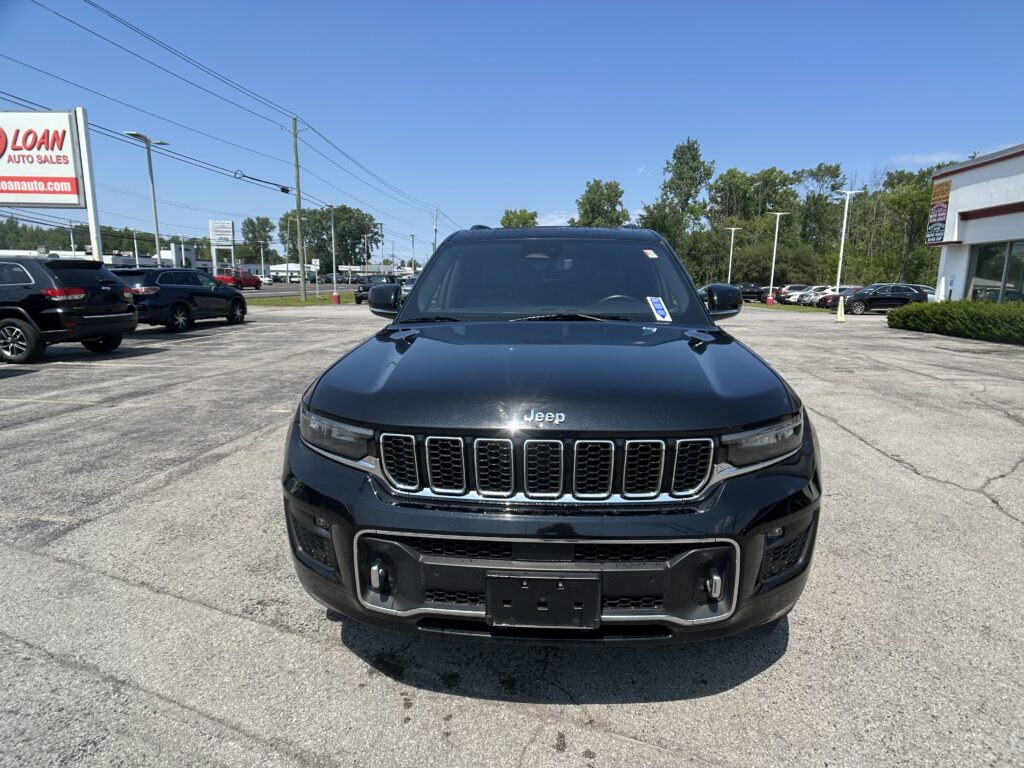 Front view of a black Jeep SUV in a car dealership lot with a blue sky and a LOAN Auto Sales sign in the background.