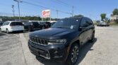 Black Jeep Grand Cherokee in a dealership lot with other cars and an EZ Loan Auto Sales sign against a clear blue sky.