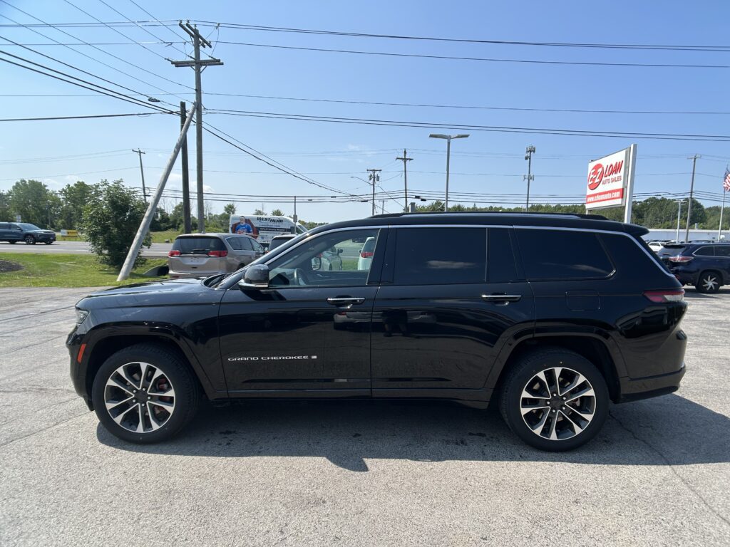 Black Grand Cherokee SUV in a dealership parking lot with utility poles and a blue sky backdrop, EZ Loan Auto Sales sign in the distance.