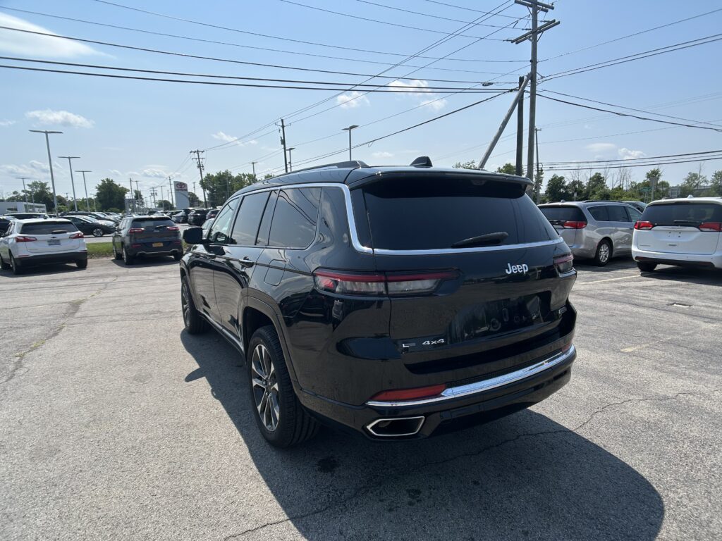 Rear view of a black Jeep SUV in a crowded parking lot with power lines overhead and a blue sky above