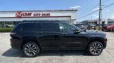 Black Jeep Grand Cherokee in a dealership lot with 'EZ LOAN AUTO SALES' sign and blue sky behind the building.