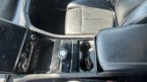 Interior of a modern car showing black leather seats, center console with a rotary gear selector, and a large touchscreen on the left side of the dash.