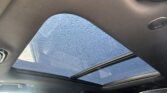 Interior of a car with the panoramic sunroof open, raindrops visible on the glass above.