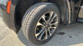 Close-up of a black vehicle's front right wheel, showing the alloy rim and tire with wheel well and suspension nearby at ground level.