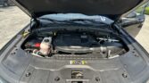 Open hood of a dark SUV (Jeep) showing the engine bay in a parking lot.