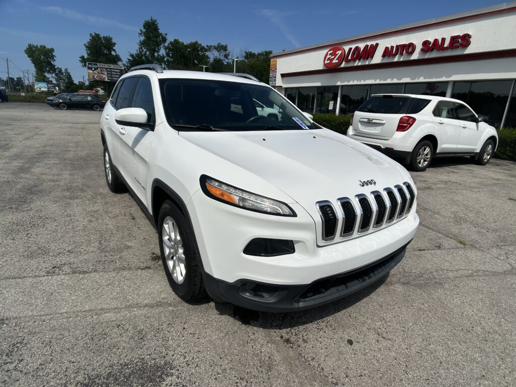 White Jeep SUV in the foreground at a car dealership lot, with the E-Z Loan Auto Sales sign on the building and other cars in the background.