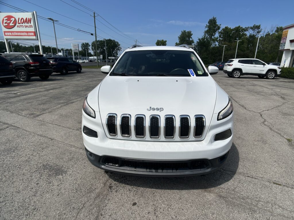 Front view of a white Jeep SUV in a car dealership lot with other vehicles and a large E-Z LOAN Auto Sales sign in the background under a blue sky.