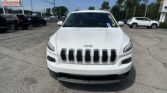 Front view of a white Jeep SUV in a car dealership lot with other vehicles and a large E-Z LOAN Auto Sales sign in the background under a blue sky.