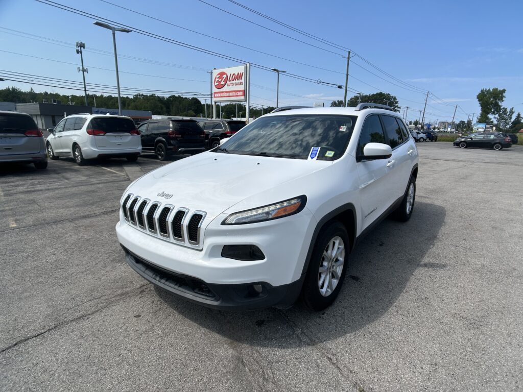 Close-up of a white Jeep SUV in a crowded dealership lot with other cars and an EZ LOAN sign in the background.