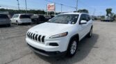Close-up of a white Jeep SUV in a crowded dealership lot with other cars and an EZ LOAN sign in the background.