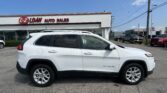 White SUV (Jeep Cherokee) parked at a car dealership with an E-Z LOAN AUTO SALES sign on the building and a clear blue sky above.