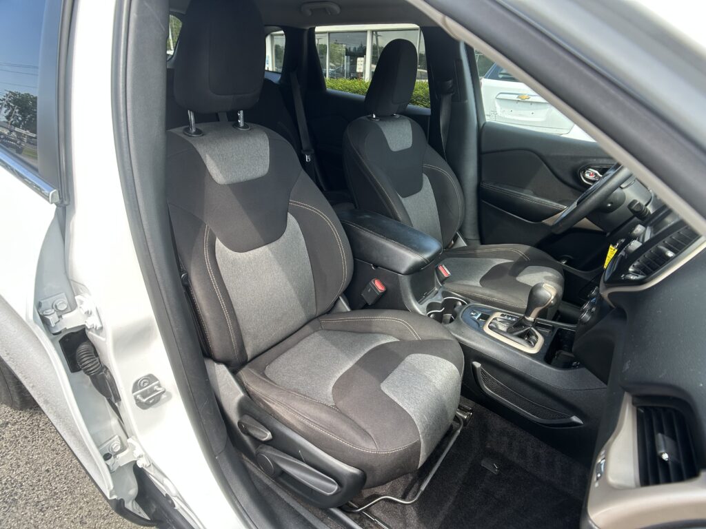Front interior of a car showing driver and passenger seats with center console and gear shifter, dark upholstery with white stitching.