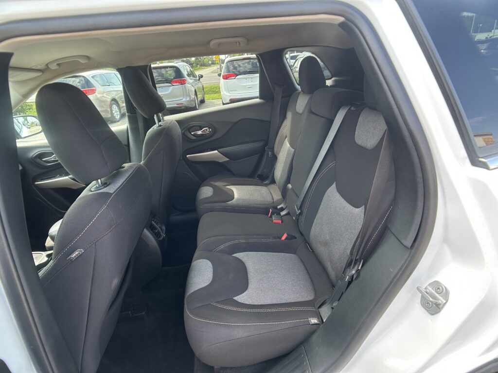 Rear passenger seating in a car: gray fabric bench with three seats, headrests, and visible seat belts
