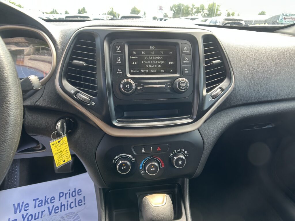 Center console infotainment screen displaying SiriusXM station 36 Alt Nation, with control buttons around and a parking lot visible through the windshield.
