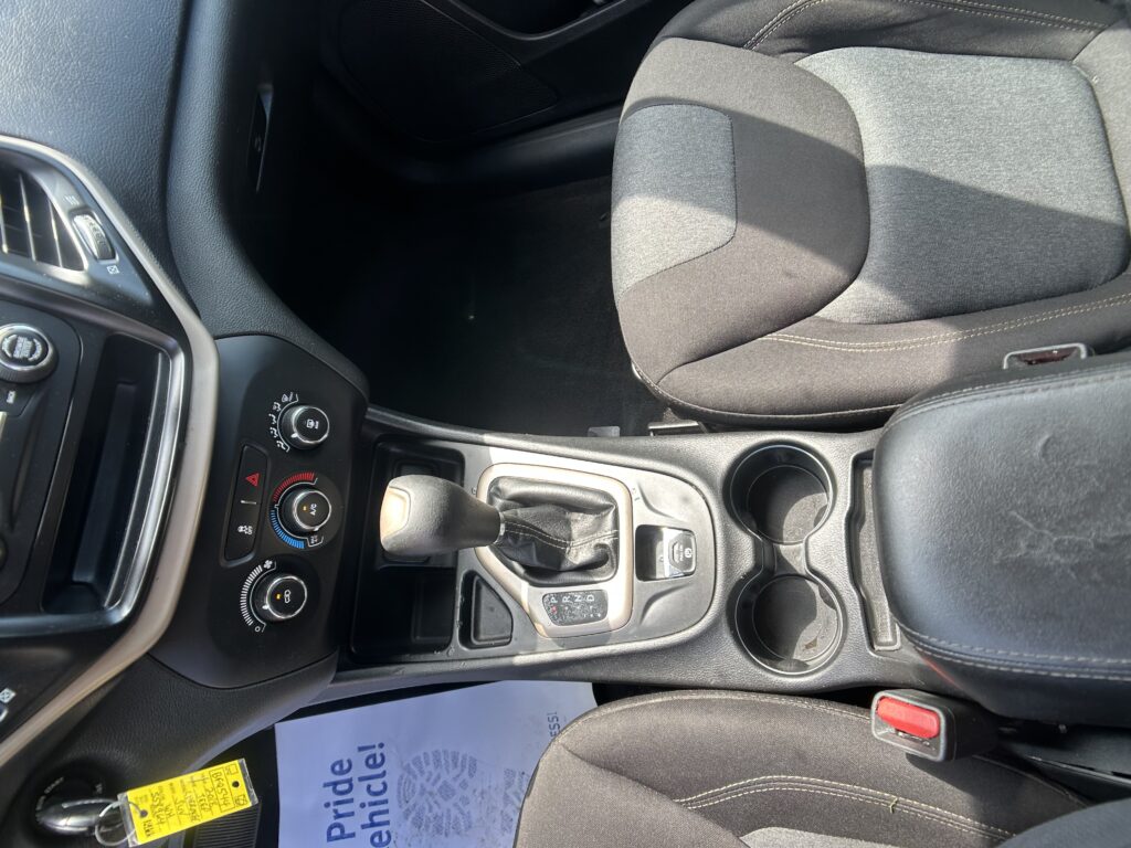 Interior of a car showing the center console with gear shifter, climate controls, cup holders, and part of the driver and passenger seats.