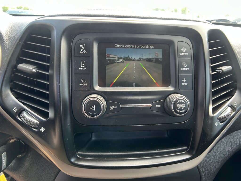 Infotainment screen shows the rearview camera with parking guidance lines (green/yellow/red) while reversing in a car interior.