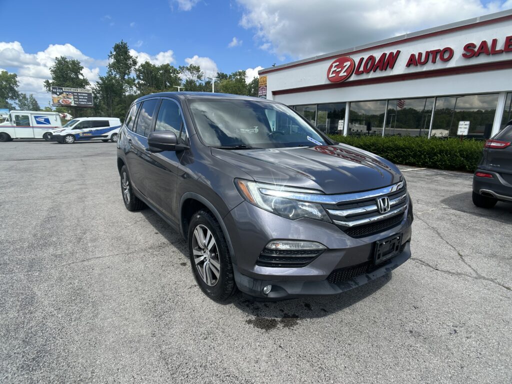 Gray Honda SUV parked in front of EZ Loan Auto Sales storefront on a sunny day with other cars and trees in the background.