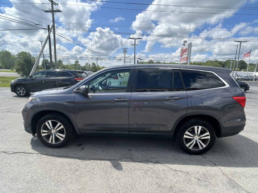 Gray SUV in a car dealership lot with another SUV nearby and power lines overhead against a blue sky with clouds.