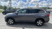 Gray SUV in a car dealership lot with another SUV nearby and power lines overhead against a blue sky with clouds.
