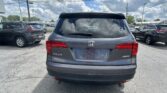 Rear view of a gray Honda Pilot in a crowded parking lot with other SUVs nearby and a cloudy sky reflected in the rear window.