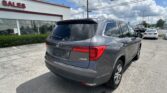 Rear three-quarter view of a gray Honda SUV in a dealership parking lot in front of a white building with a red 'SALES' sign, blue sky above.