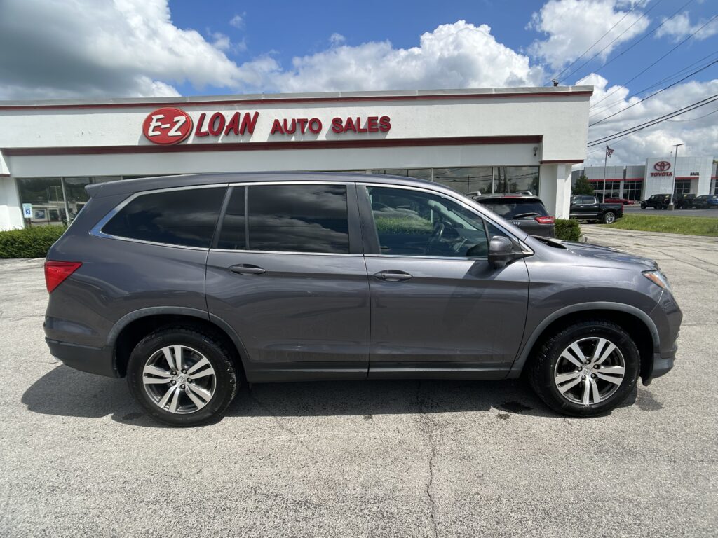 Gray SUV parked in front of a white auto dealership sign reading 'E-Z LOAN AUTO SALES' under a blue sky with clouds