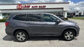 Gray SUV parked in front of a white auto dealership sign reading 'E-Z LOAN AUTO SALES' under a blue sky with clouds