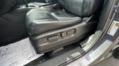Black leather front passenger seat with visible seat controls on the side, center console and gear shifter in view; car door open with a yellow warning label along the door frame.