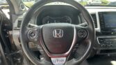 Driver's view of a black leather steering wheel with Honda emblem, instrument cluster, and center console, looking out at a busy parking lot through the windshield.