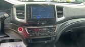 Center touchscreen in a car showing FM radio 96.9 and tuning options, with outside dealership lot visible through windshield.