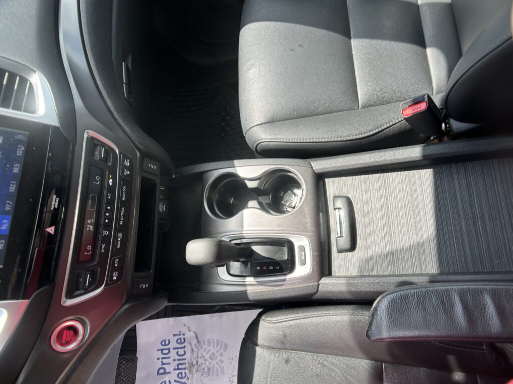 Interior of a car showing the center console with cup holders, gear shifter, and passenger seat belt buckle nearby.