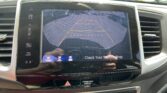 In-dash display showing the car's rearview camera with orange guiding lines for backing into a parking spot, visible parking lot in the background.