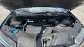Car hood open, view into the engine bay with the blue coolant cap on the left and various engine components visible.