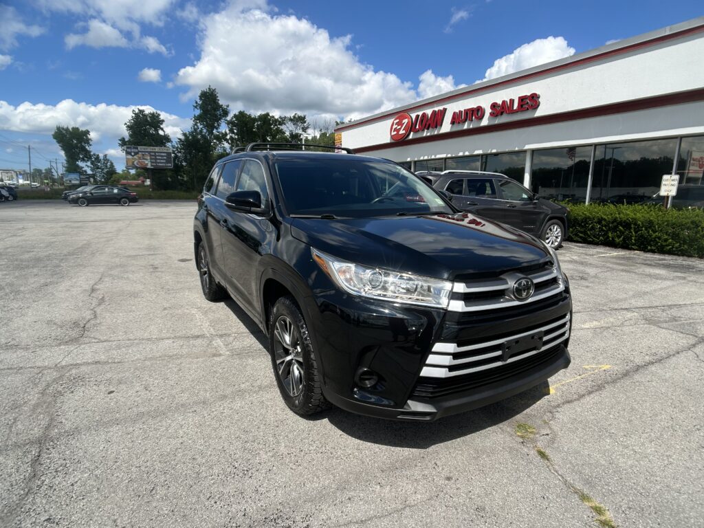 Black SUV parked in front of a white auto dealership building with a red LOAN AUTO SALES sign on a sunny day.